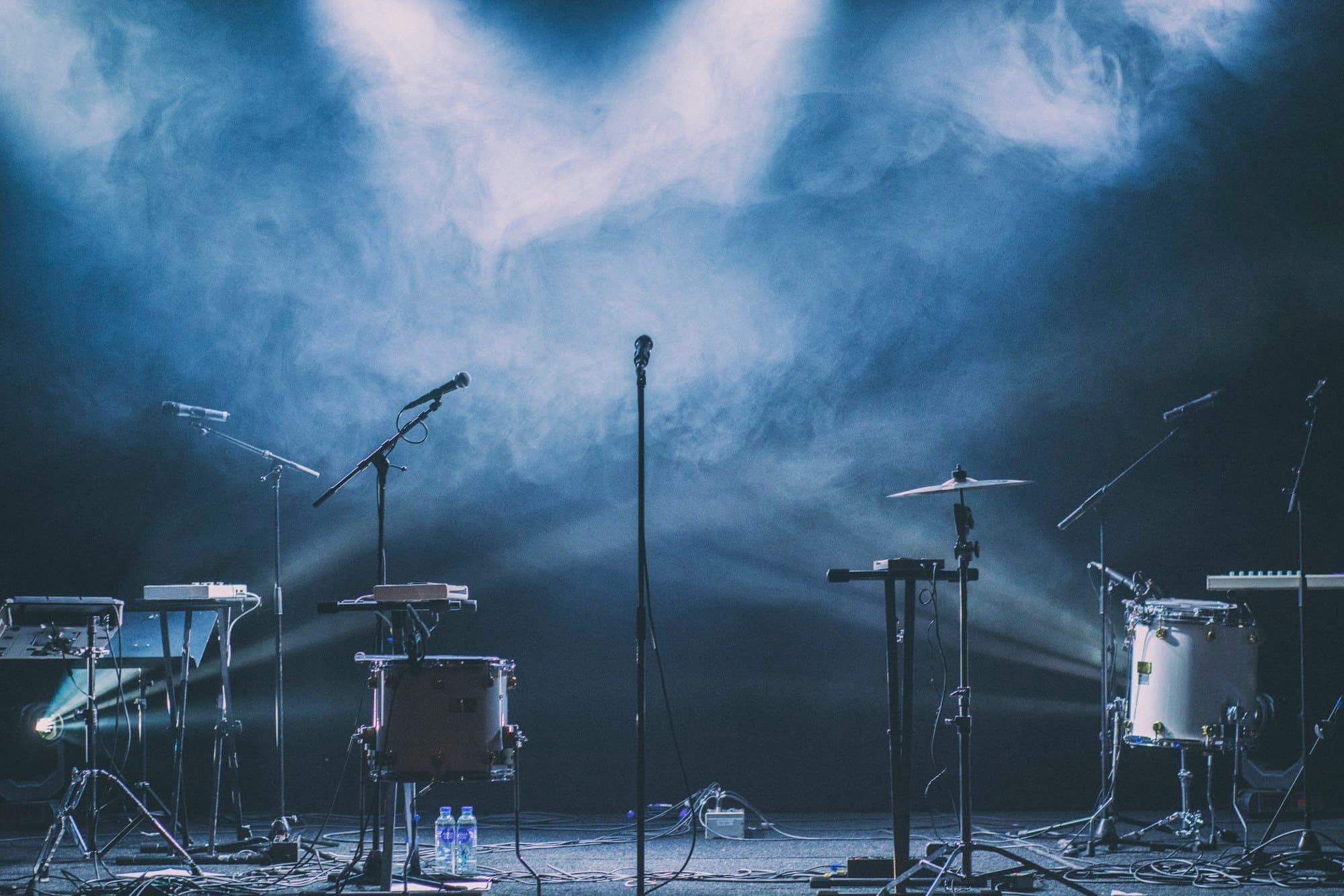 Une scène de salle de concert avant l’ouverture : les instruments sont installés, personne encore, deux projecteurs découpent la fumée.